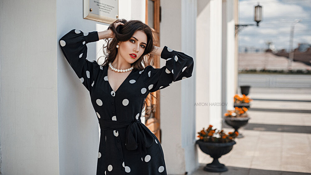 Обои для рабочего стола Модель Мария Башмакова в черном платье в белый горох стоит у стены дома, фотограф Харисов Антон