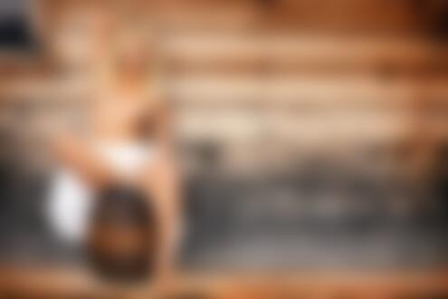 Обои на рабочий стол Блондинка в приспущенном платье топлес сидит на бочонке у стены деревянного дома