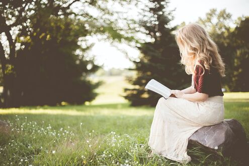 Обои на рабочий стол Девушка - блондинка сидит на камне и читает книгу