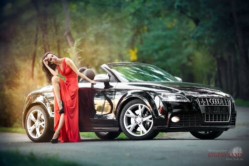 Обои на рабочий стол Красотка в длинном красном платье стоит, облокотившись на Audi TT Cabrio черного цвета посреди лесной дороги
