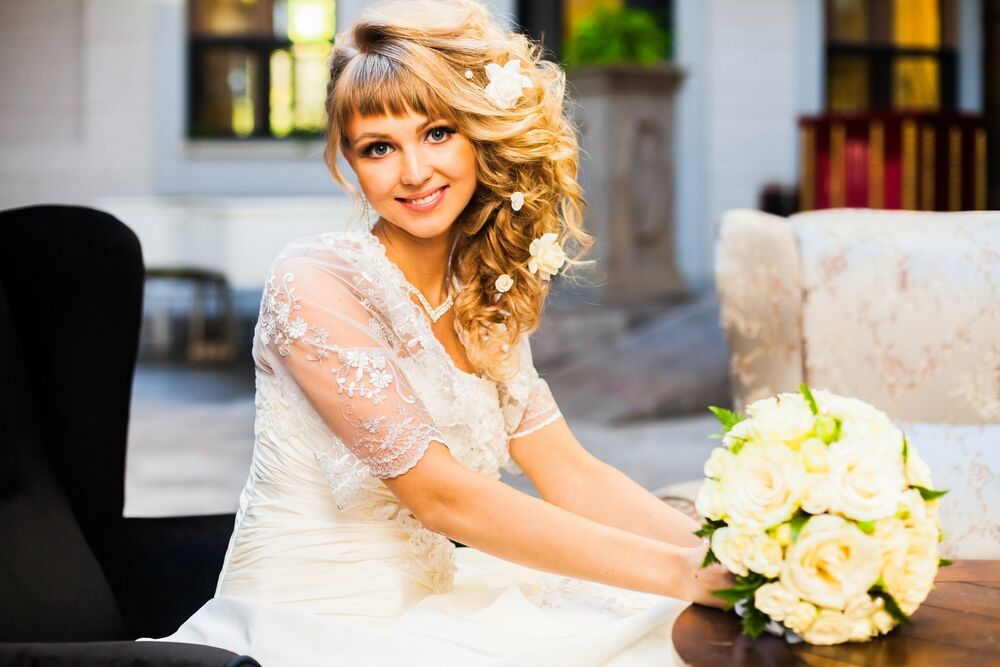 Обои для рабочего стола Белокурая блондинка в свадебном платье сидит у столика с букетом цветов