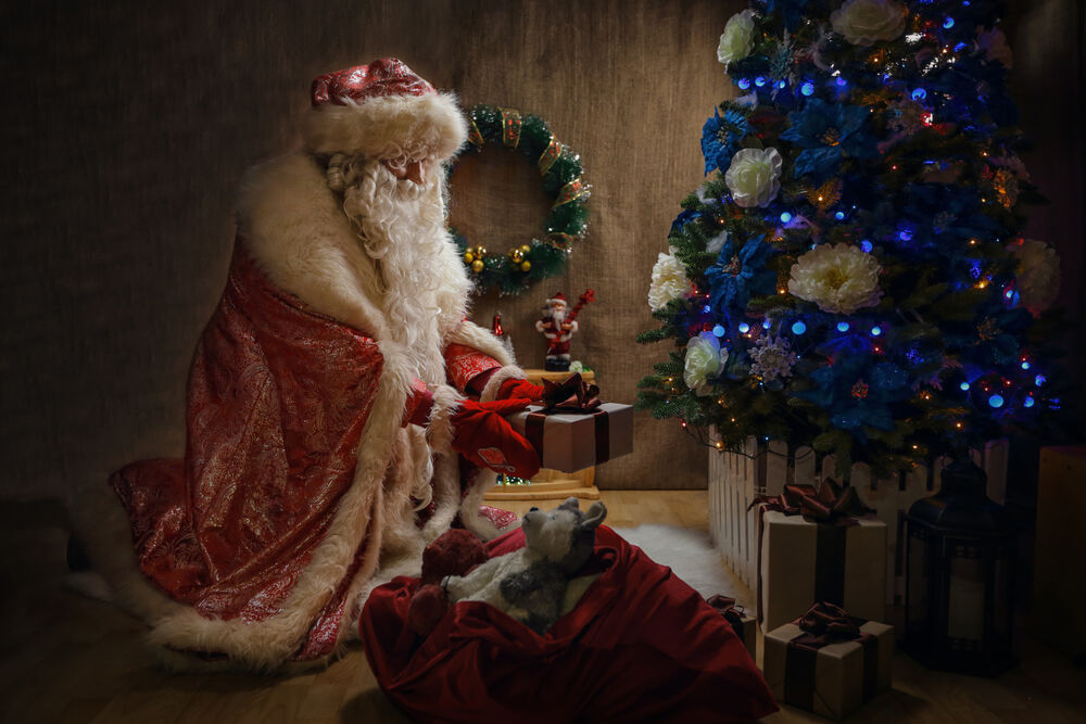 Обои для рабочего стола Дед Мороз раскладывает подарки под елкой