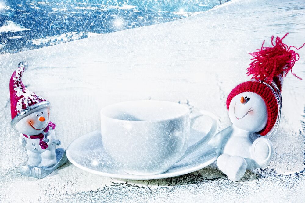 Обои для рабочего стола Два игрушечных снеговика на снежном склоне у белой чашки