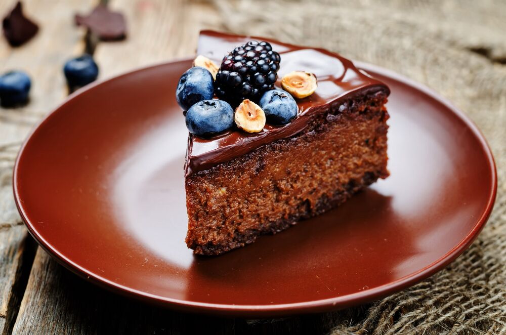 Обои для рабочего стола Кусок шоколадного пирога со свежими ягодами черники и ежевики на тарелке