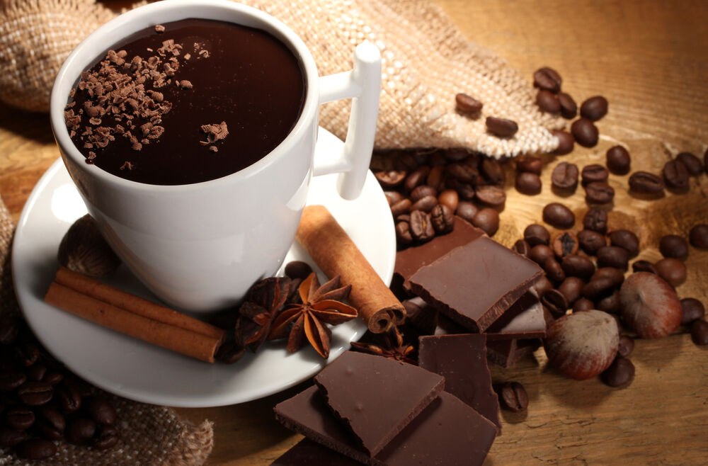 Обои для рабочего стола Чашка кофе с корицей на блюдце стоит посреди кофейных зерен и кусочков шоколада