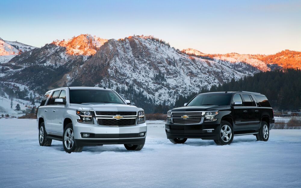 Обои для рабочего стола Два авто Chevrolet Suburban, серебристого и черного цвета, стоят на снегу на фоне гор