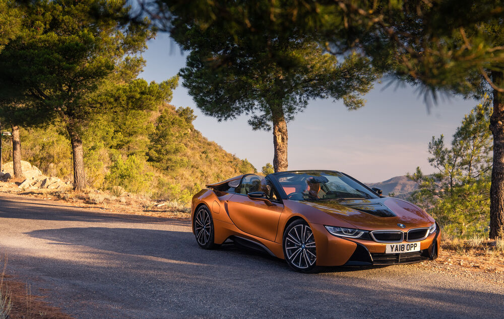 Обои для рабочего стола BMW I8 Cabrio в золотом цвете стоит на горной дороге на фоне деревьев