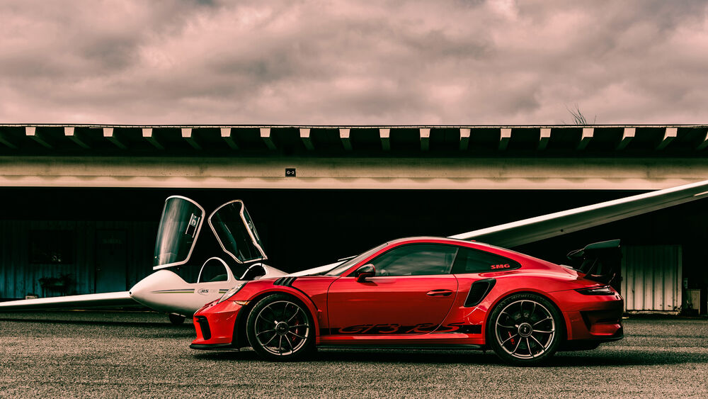 Обои для рабочего стола Porshe 911 GTS RS красного цвета стоит на фоне ангара с планером