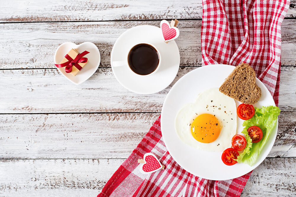Обои для рабочего стола Завтрак ко Дню Святого Валентина: чашка кофе, яичница, салат, помидоры черри, хлеб и лист салата. С подарком и сердечками на белых досках