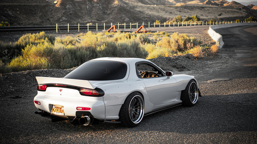 Обои для рабочего стола Белая Mazda RX-7 стоит на дороге в горной местности