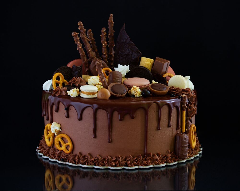 Обои для рабочего стола Шоколадный торт украшенный печеньем, трубочками и крендельками на черном фоне