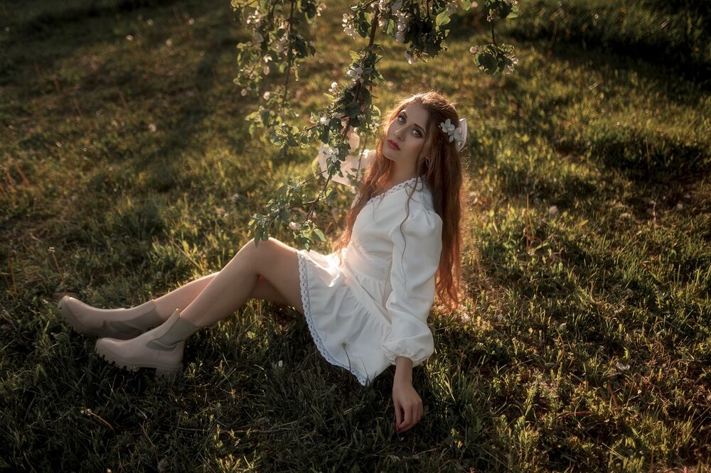 Обои для рабочего стола Девушка Вита Воротилина с длинными волосами в белом платье сидит на траве под ветвями цветущего дерева
