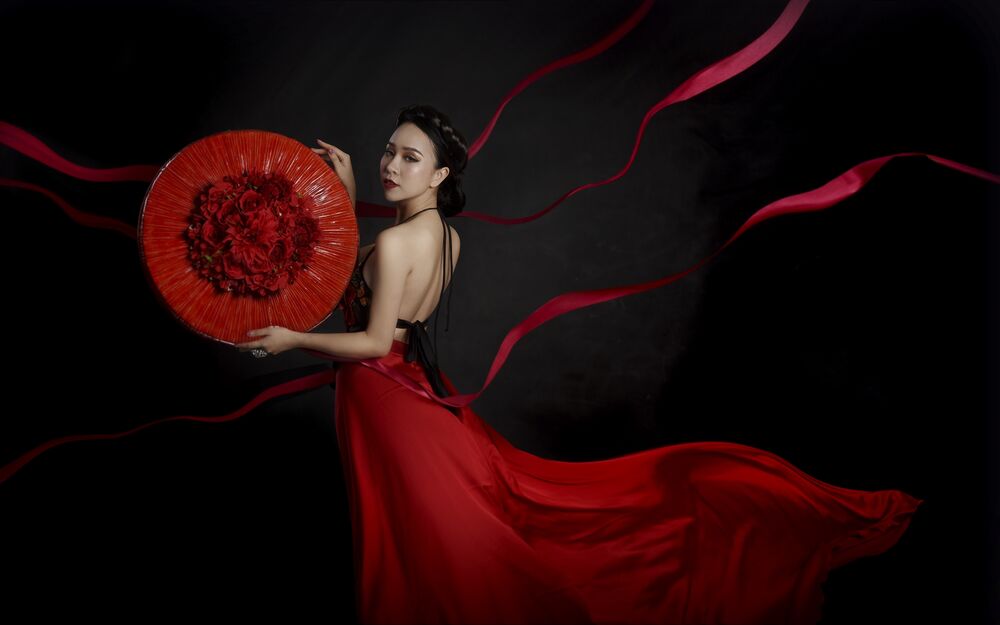 Обои для рабочего стола Азиатская девушка в красном платье с красным кругом в руках на черном фоне с красными лентами