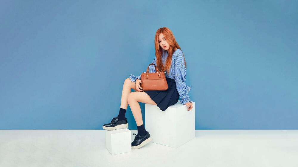Обои для рабочего стола Розэ / Rose из музыкальной группы Блэкпинк / Blackpink с сумочкой и в юбке позирует на голубом фоне
