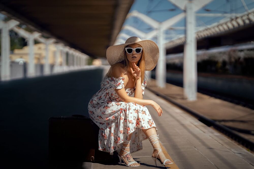 Обои для рабочего стола Модель Марина Макарова в шляпе, в темных очках и в цветастом платье сидит на чемодане на перроне вокзала