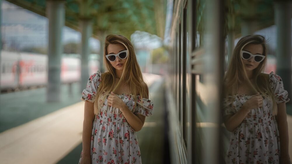 Обои для рабочего стола Модель Марина в темных очках и в цветастом платье стоит у вагона поезда на перроне вокзала