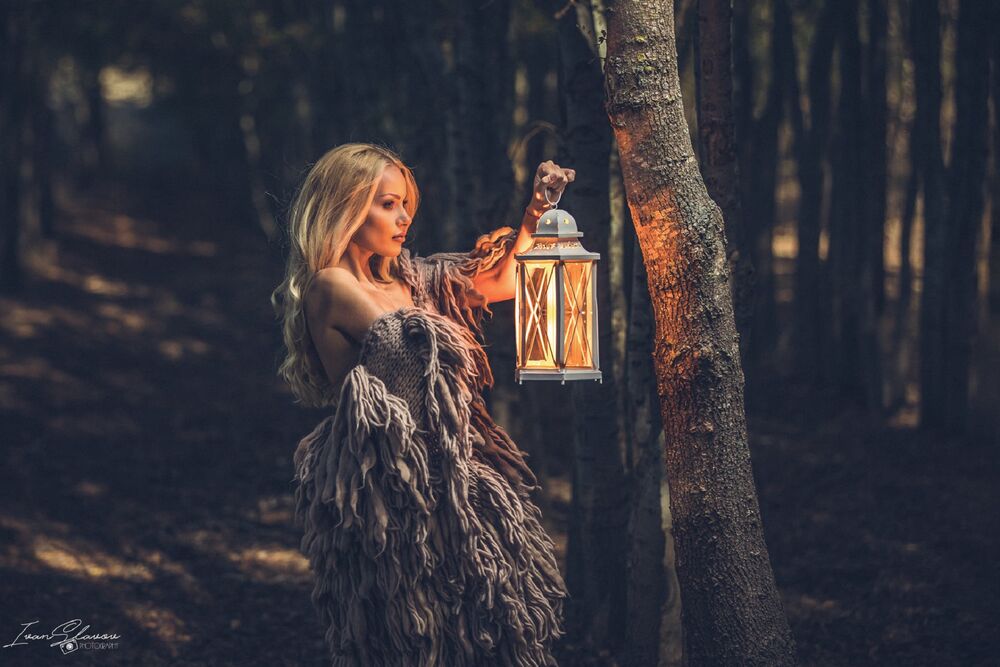 Обои для рабочего стола Девушка - блондинка с горящим фонарем в руке стоит в лесу