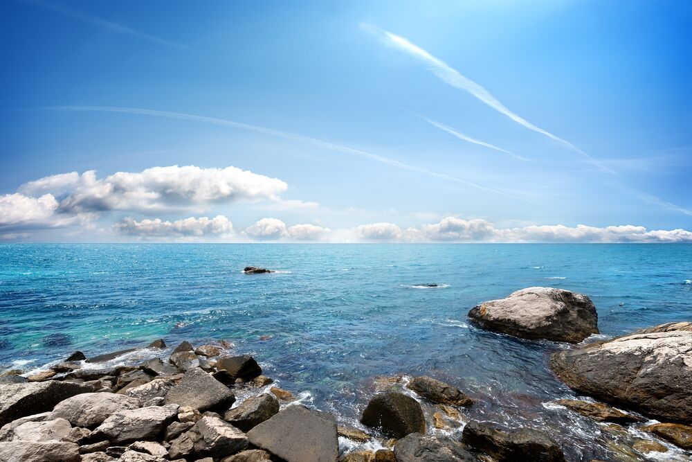Обои для рабочего стола Каменистый берег голубого моря под голубым небом с редкими облаками