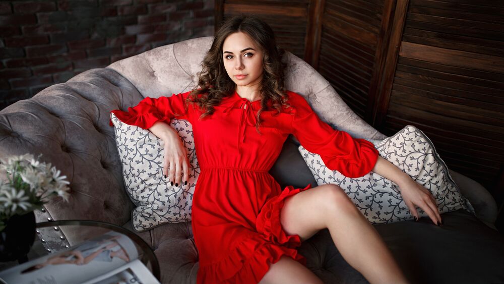 Обои для рабочего стола Модель Anastasia в красном платье сидит на диване в комнате