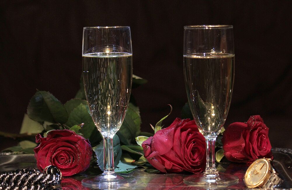 Обои для рабочего стола Два бокала с шампанским стоят рядом с бордовыми розами и часами