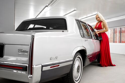 Обои на рабочий стол Блондинка в красном длинном платье стоит у авто Cadillac DeVille в гаражном помещении