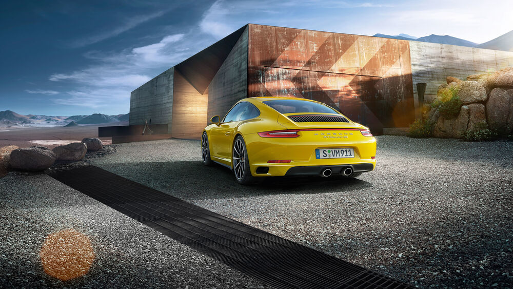 Обои для рабочего стола Автомобиль желтого цвета Porsche 911 Carrera 4S, стоит возле строений и каменных глыб в долине на фоне гор и неба