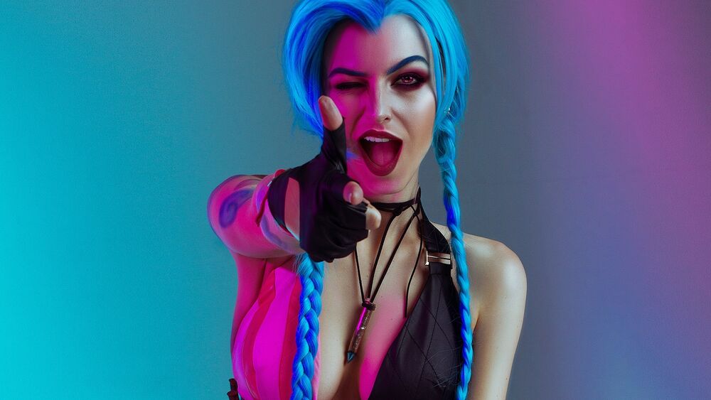 Обои для рабочего стола Косплей Jinx / Джинкс, персонаж из видеоигры League of Legends / Лига Легенд на розовом фоне указывает рукой изображая пистолет