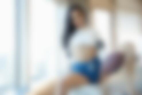Обои на рабочий стол Модель Emily Willis позирует сидя на краю дивана в белой кофточке и синих шортах, держа в руке мяч для регби