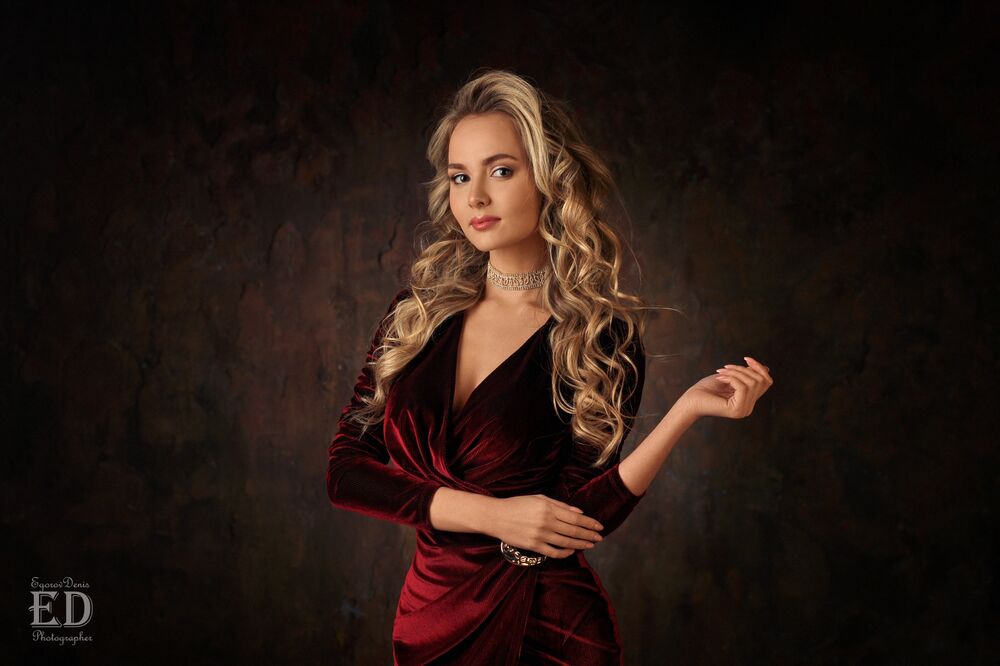 Обои для рабочего стола Модель Katya Khalpert / Катя Халперт позирует стоя в бордовом бархатном платье, на фоне темной стены