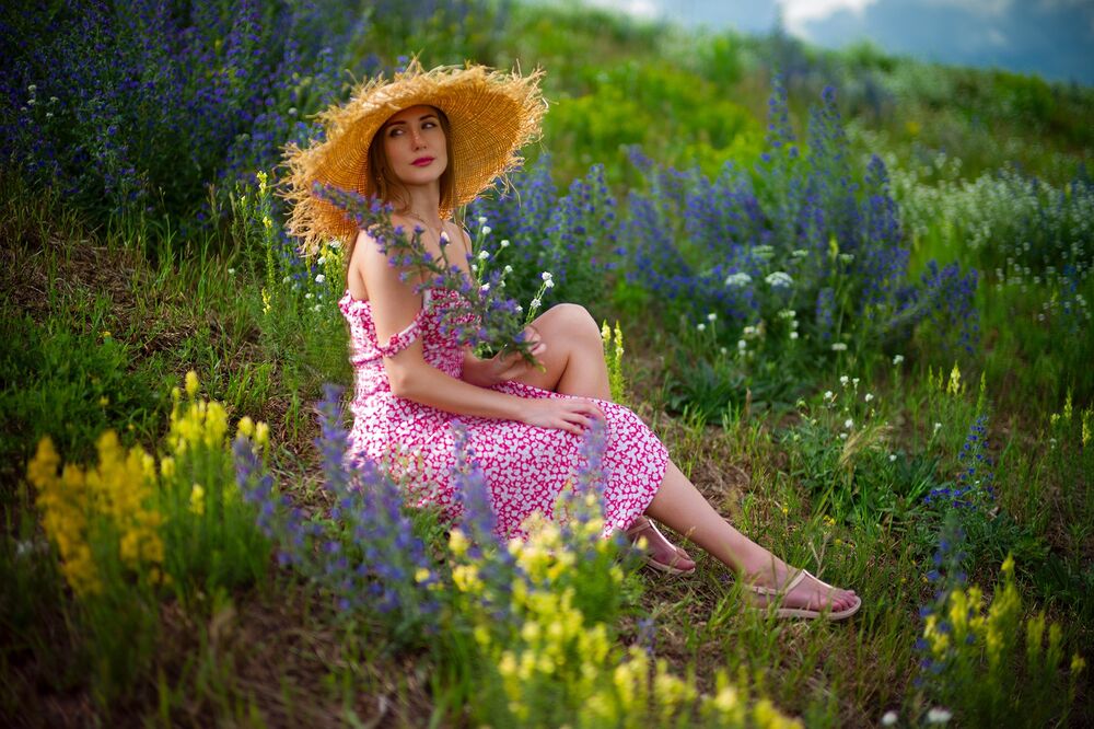 Обои для рабочего стола Девушка в пятнистом платье с открытыми плечами сидит в поле с цветами