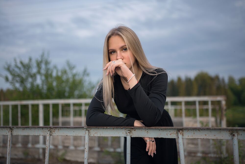 Обои для рабочего стола Модель Аня в черном платье стоит у ограждения на природе