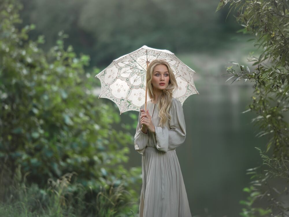 Обои для рабочего стола Блондинка в сером длинном платье и с зонтом в руках стоит на берегу водоема