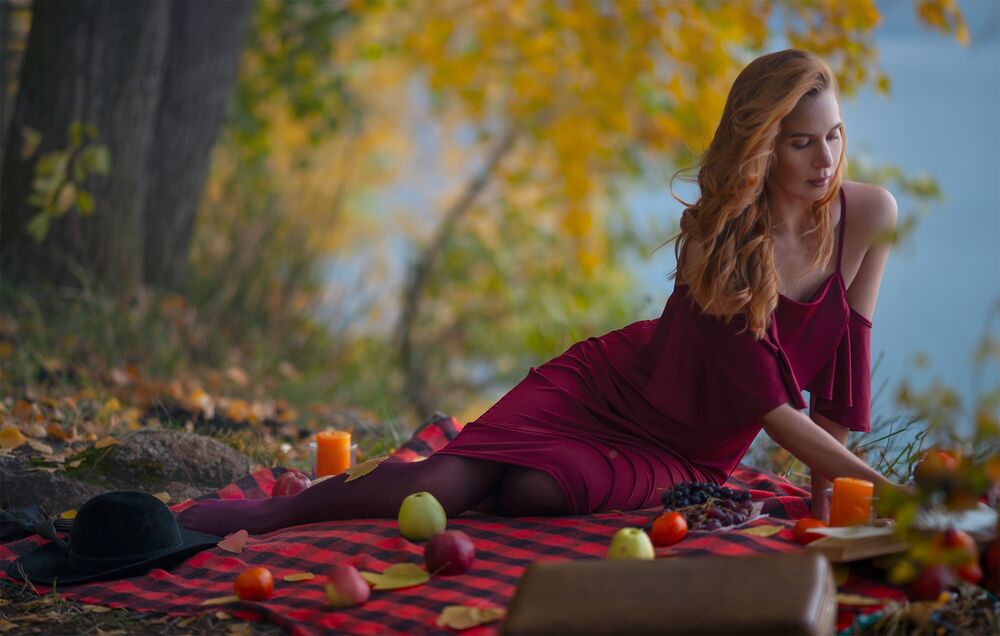 Обои для рабочего стола Рыжеволосая девушка в бордовом платье сидит на клетчатом покрывале с фруктами на природе