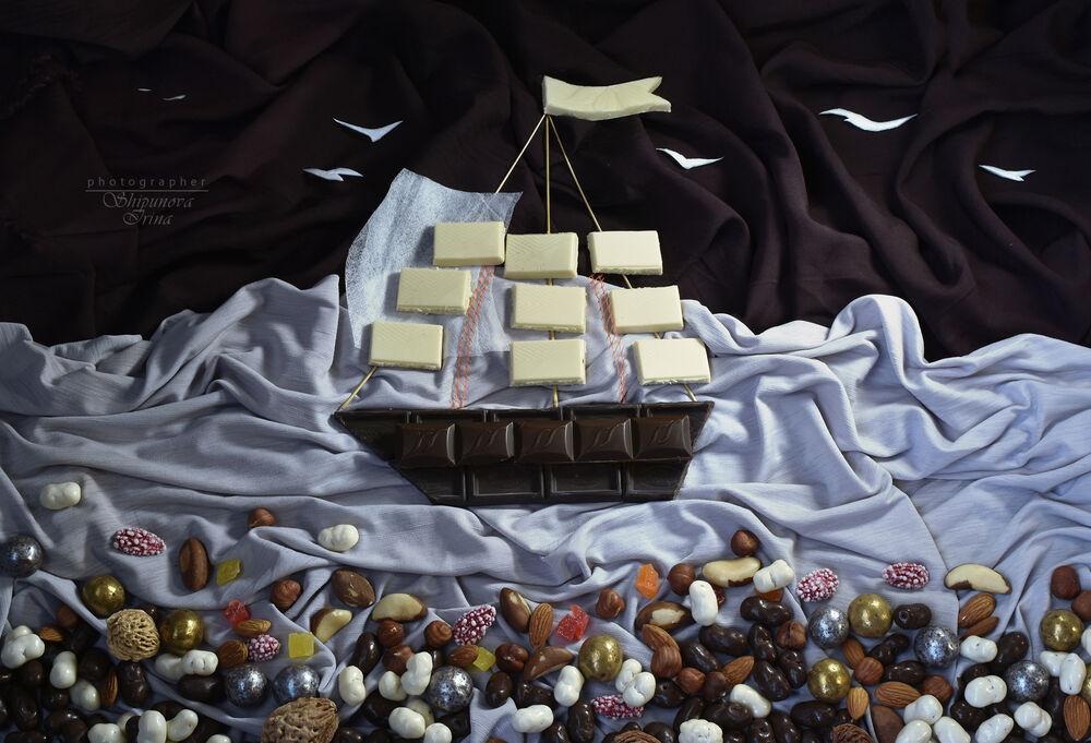 Обои для рабочего стола Корабль из шоколада на белой ткани украшенный снизу конфетами
