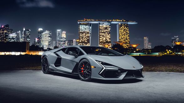 Обои на рабочий стол Серый 2024 Lamborghini Revuelto ночью на фоне Гостиница с казиноМарина-Бей Сэндс в Сингапуре
