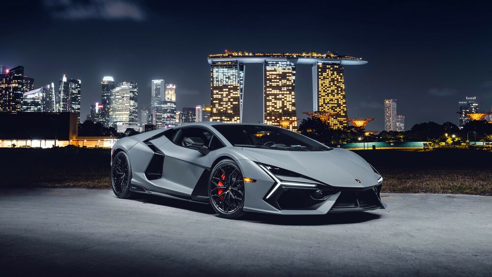 Обои для рабочего стола Серый 2024 Lamborghini Revuelto ночью на фоне Гостиница с казиноМарина-Бей Сэндс в Сингапуре