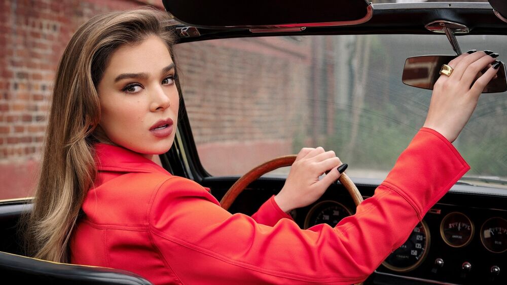 Обои для рабочего стола Hailee Steinfeld в красном пальто оборачивается за рулем машины поправляя зеркало