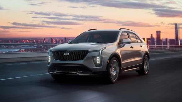 Обои на рабочий стол Темный Cadillac XT4 Sport 2023 на городской эстакаде на фоне города на закате
