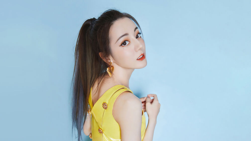 Обои для рабочего стола Дилраба Дилмурат / Dilraba Dilmurat в желтом платье с золотыми серьгами в форме сердца на голубом фоне