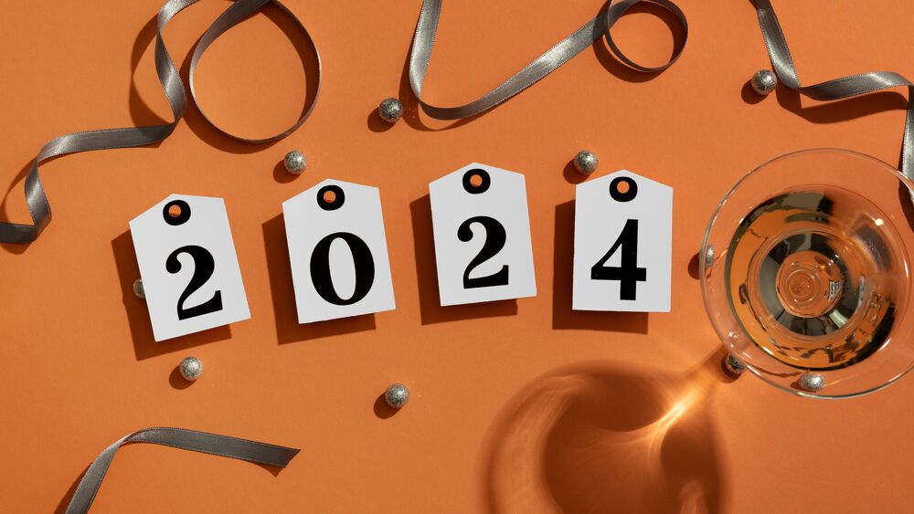 Обои для рабочего стола Цифры 2024 на бирках рядом с бокалом шампанского на оранжевом фоне