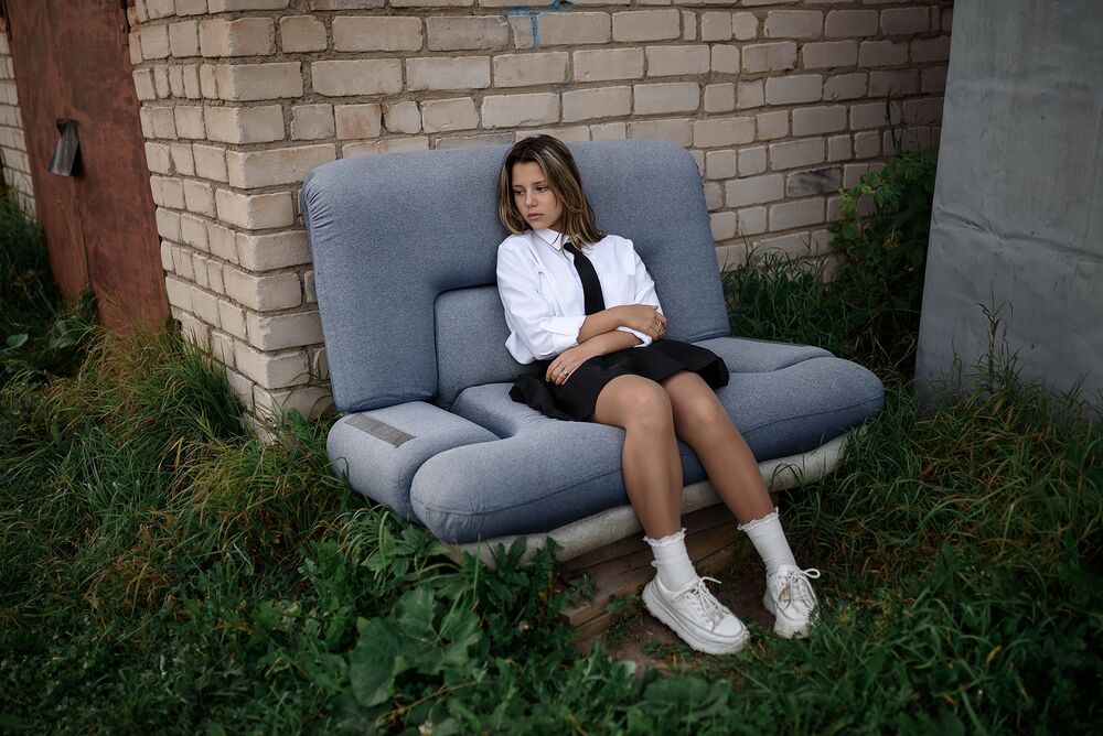 Обои для рабочего стола Модель Карина в белой рубашке с галстуком и в юбке сидит на диване у кирпичной стены здания