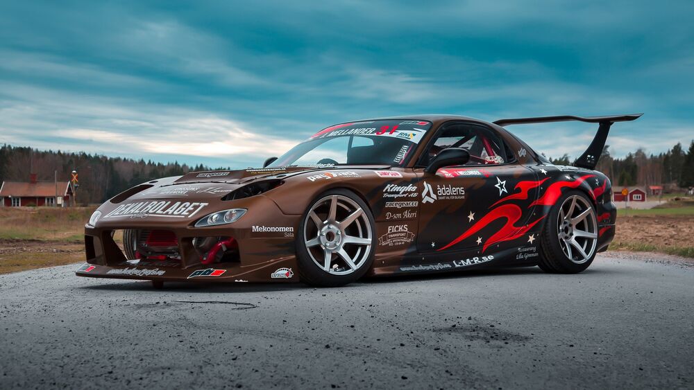 Обои для рабочего стола Коричневая Mazda RX-7 под серым небом на бетоне