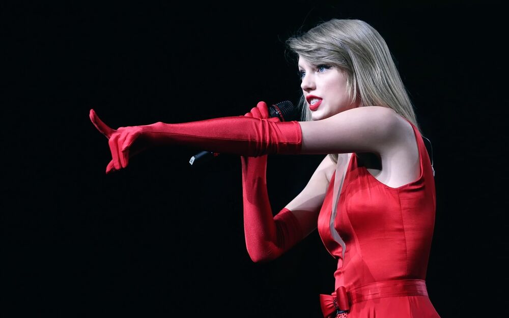 Обои для рабочего стола Taylor Swift / Тейлор Свифт в красном платье и перчатках поет в микрофон на черном фоне