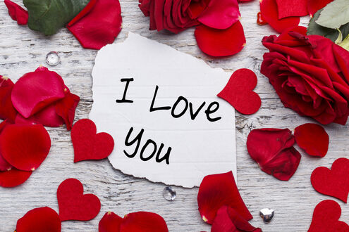 Обои на рабочий стол Бумага с надписью I love you среди красных лепестков роз на белом фоне