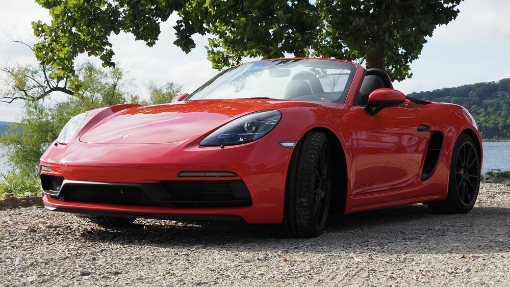Обои для рабочего стола Красная машина Porsche Boxster стоит на дороге на фоне деревьев и реки и неба