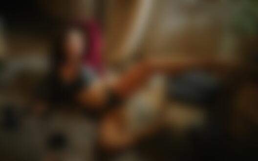 Обои для рабочего стола Темноволосая девушка в распахнутой бордовой кофточке и в черном кружевном нижнем белье лежит на полу комнаты, положив ногу на стул