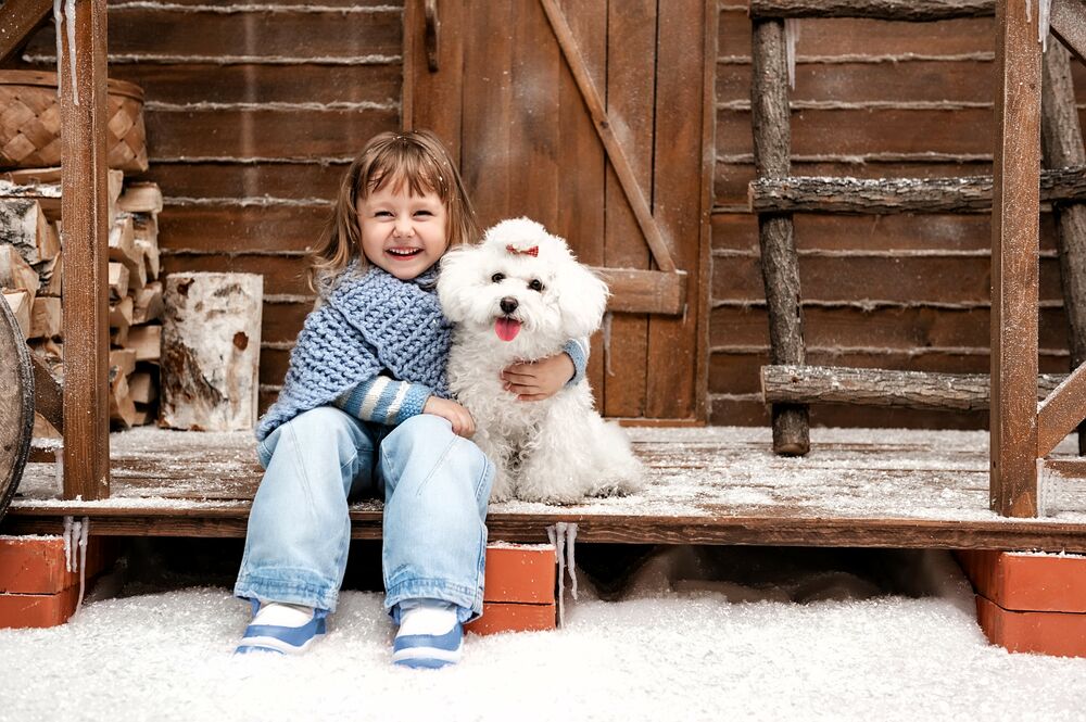 Обои для рабочего стола Девочка с собачкой сидит на заснеженном крыльце деревянного дома