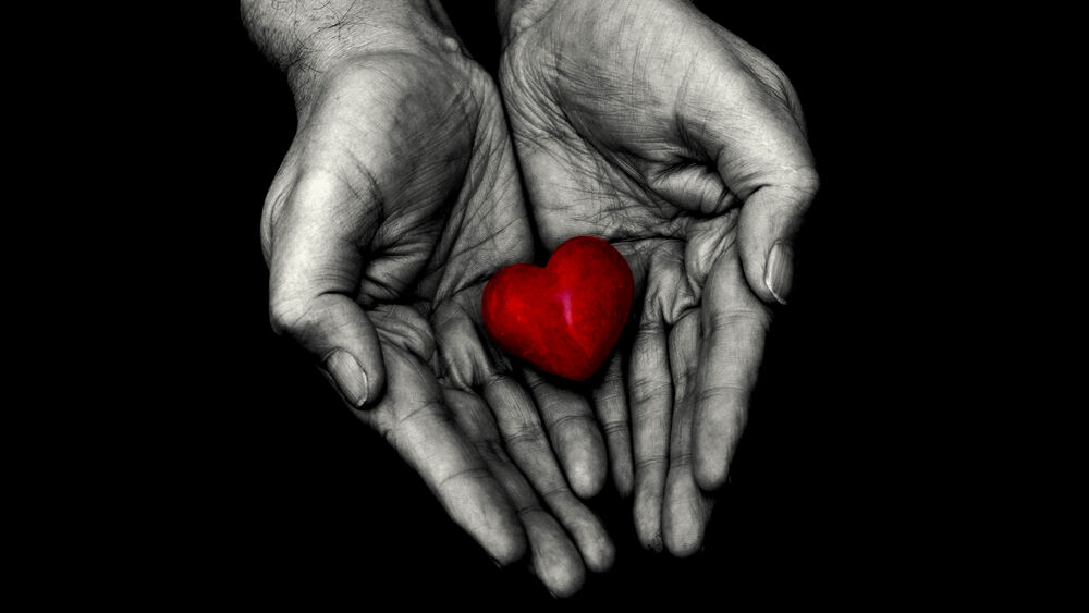 Обои для рабочего стола Красное сердце в руках на черном фоне