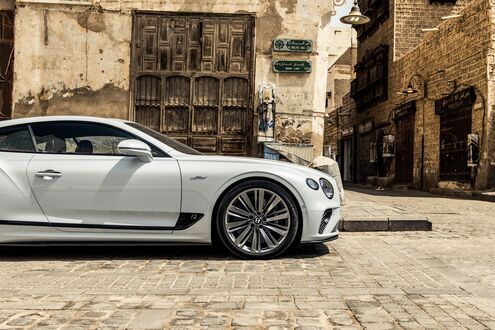 Обои на рабочий стол Белый автомобиль Bentley Continental GT Speed на фоне коричневой улицы города
