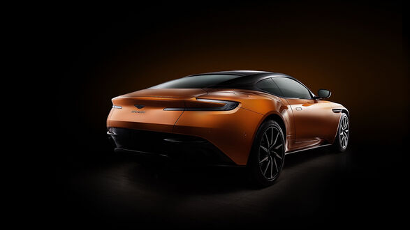 Обои на рабочий стол Рыжий автомобиль Aston Martin на черном фоне сзади